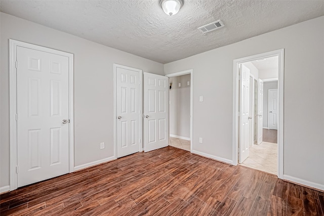 unfurnished bedroom with visible vents, a textured ceiling, baseboards, and wood finished floors