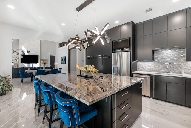 kitchen with a center island, marble finish floor, a breakfast bar area, stainless steel appliances, and a sink