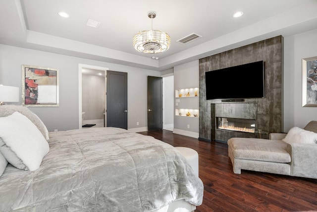 bedroom with baseboards, visible vents, a raised ceiling, a tiled fireplace, and wood finished floors