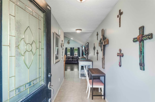 corridor featuring lofted ceiling, a textured ceiling, baseboards, and light tile patterned floors