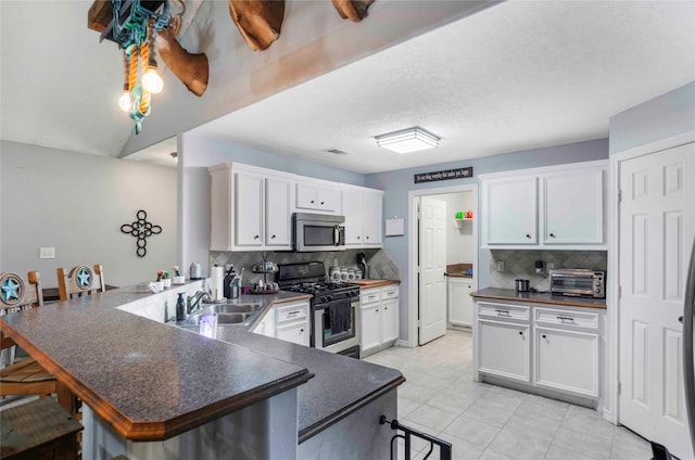 kitchen with a toaster, gas range oven, a peninsula, stainless steel microwave, and dark countertops