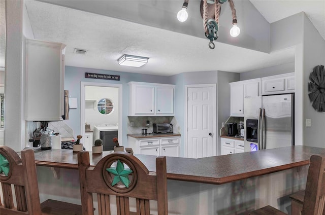 kitchen with dark countertops, a peninsula, stainless steel refrigerator with ice dispenser, and backsplash