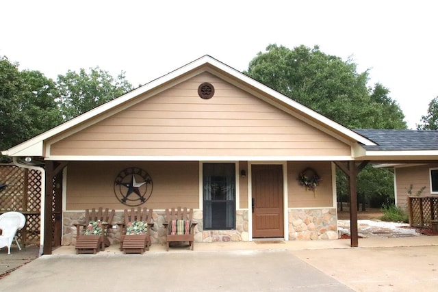 view of front of house featuring stone siding, a porch, and roof with shingles