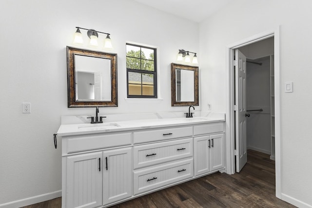 full bathroom with double vanity, wood finished floors, a sink, and baseboards