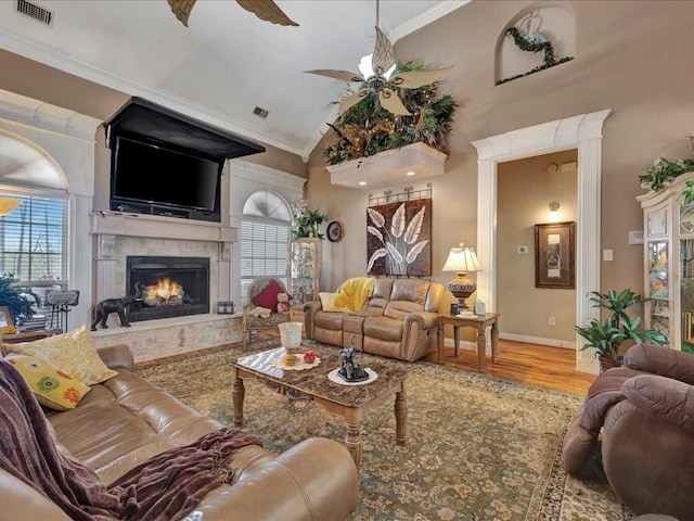 living room featuring crown molding, visible vents, ceiling fan, wood finished floors, and a lit fireplace