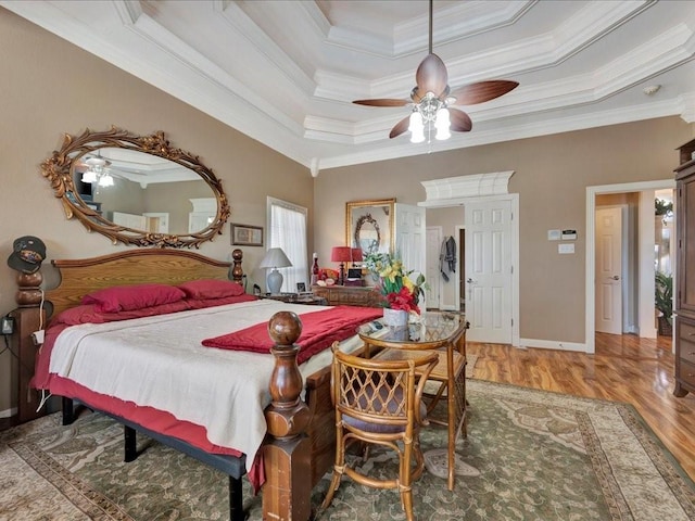 bedroom featuring a raised ceiling, light wood-style flooring, ornamental molding, ceiling fan, and baseboards