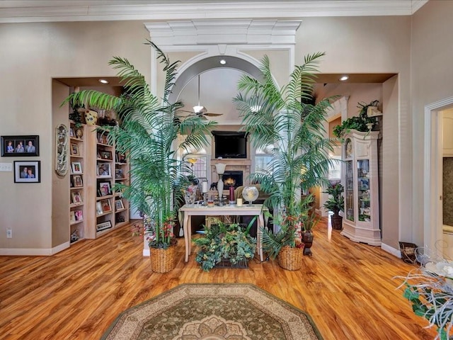 interior space with crown molding, ceiling fan, wood finished floors, a lit fireplace, and baseboards