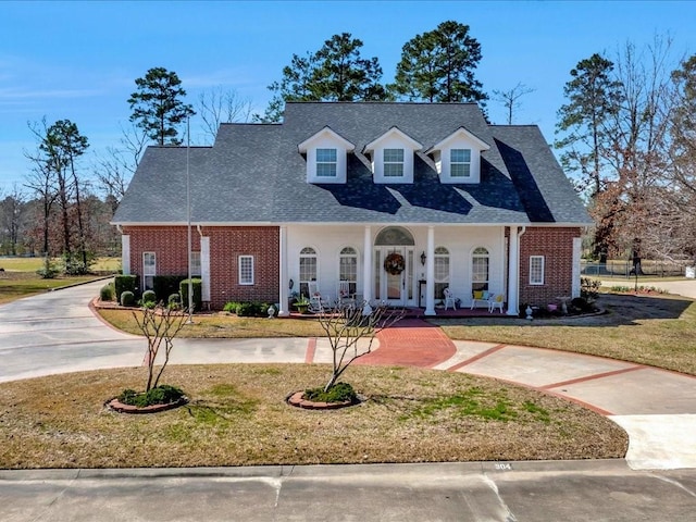 view of front of home featuring covered porch, a shingled roof, a front lawn, and brick siding