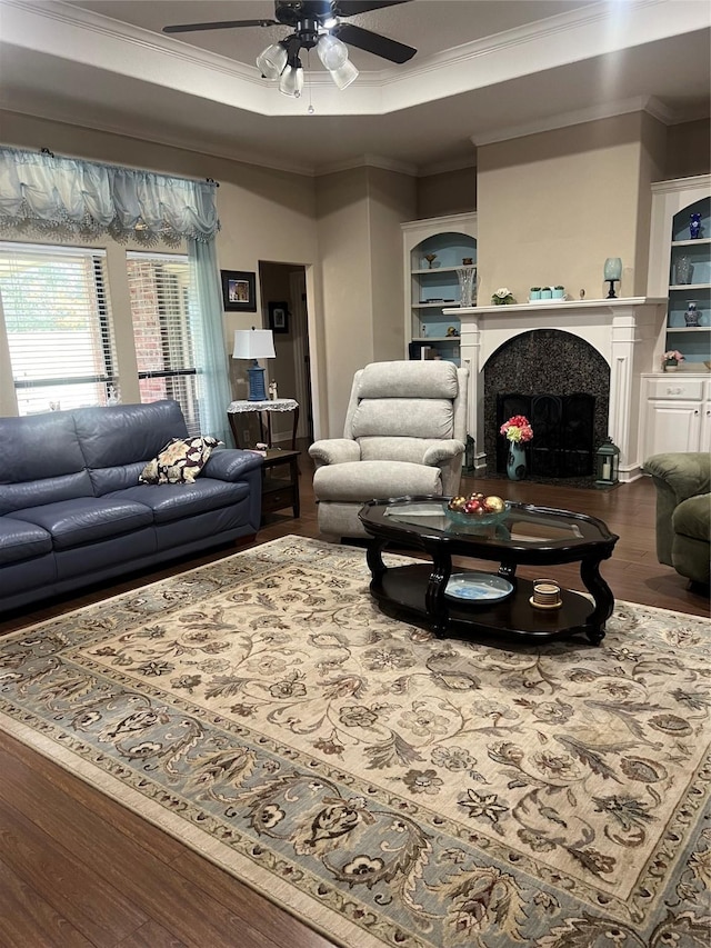 living area with built in features, ornamental molding, wood finished floors, a tray ceiling, and a fireplace