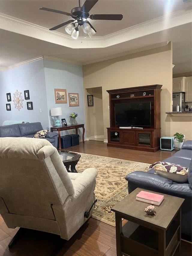 living room with ceiling fan, ornamental molding, a raised ceiling, and wood finished floors