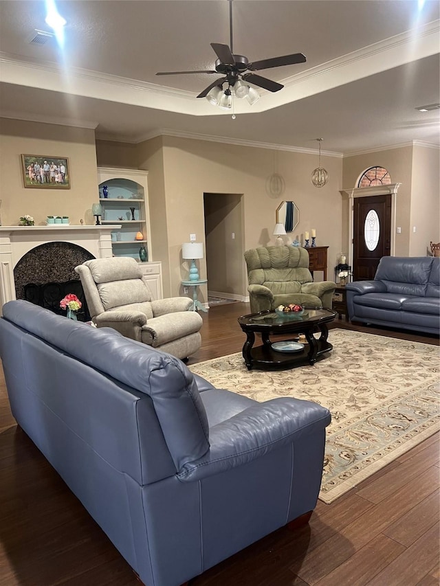 living area featuring a fireplace, a raised ceiling, dark wood-type flooring, ornamental molding, and a ceiling fan