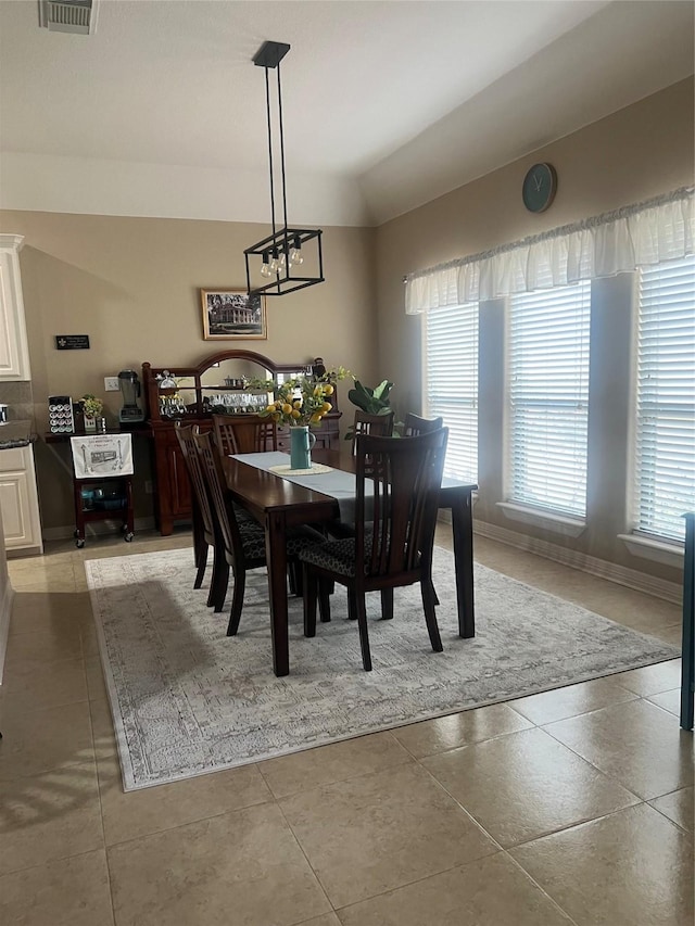 dining room with baseboards, visible vents, vaulted ceiling, and tile patterned flooring