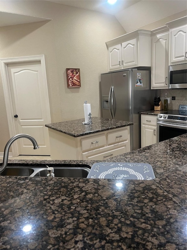 kitchen with decorative backsplash, appliances with stainless steel finishes, white cabinets, a sink, and dark stone countertops