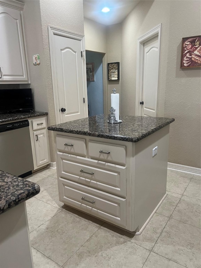 kitchen with baseboards, dark stone counters, a center island, white cabinetry, and stainless steel dishwasher