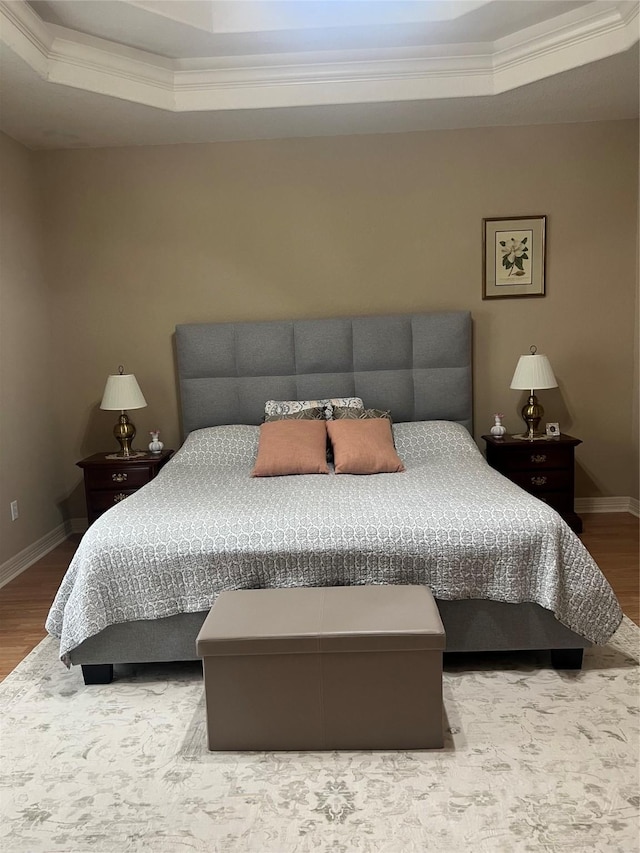 bedroom featuring a tray ceiling, wood finished floors, and baseboards