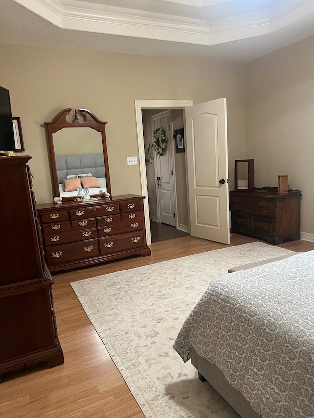 bedroom featuring light wood-type flooring, a tray ceiling, and crown molding