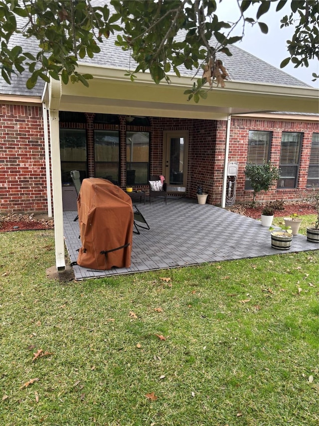 rear view of house with a patio area, brick siding, a yard, and roof with shingles