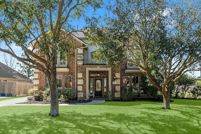 view of front of house with brick siding, a front yard, fence, and a balcony