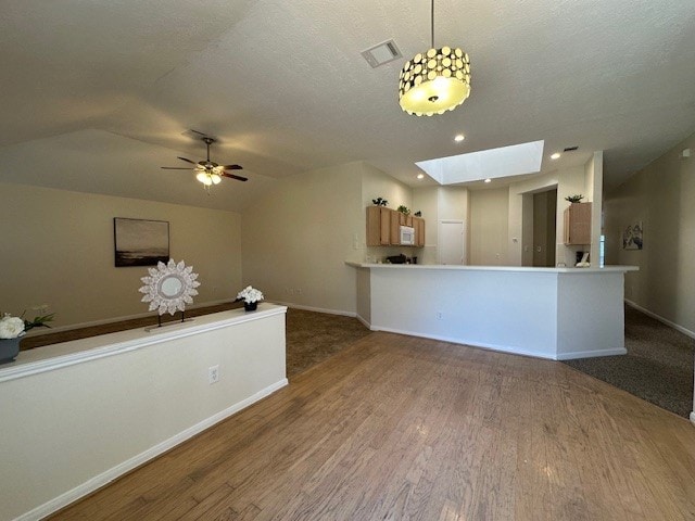 interior space with baseboards, vaulted ceiling with skylight, visible vents, and wood finished floors