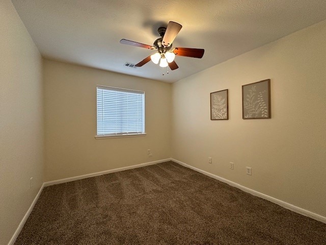 empty room with baseboards, visible vents, dark colored carpet, and a ceiling fan