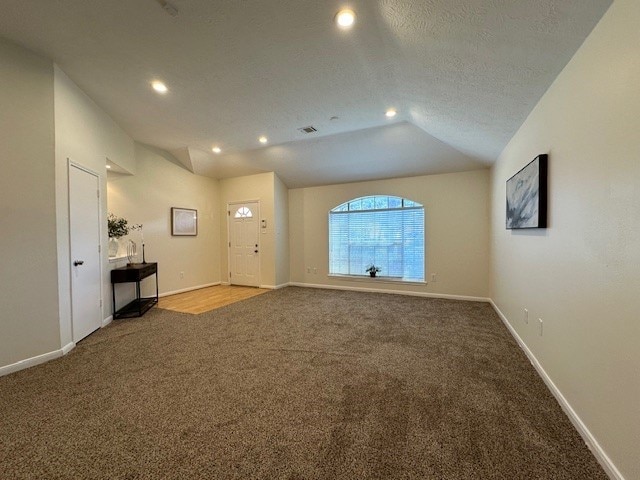 unfurnished living room featuring visible vents, carpet flooring, vaulted ceiling, a textured ceiling, and baseboards