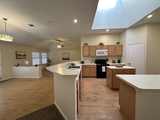 kitchen with a center island, light countertops, black gas range oven, white microwave, and a peninsula