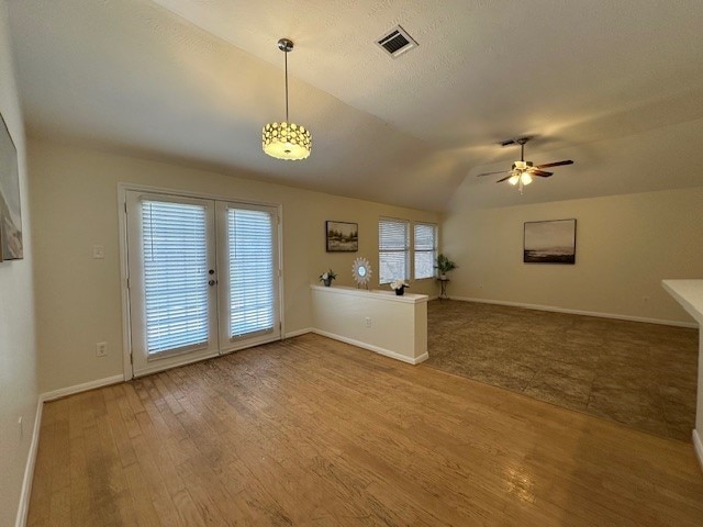 unfurnished living room with visible vents, a ceiling fan, vaulted ceiling, wood finished floors, and baseboards