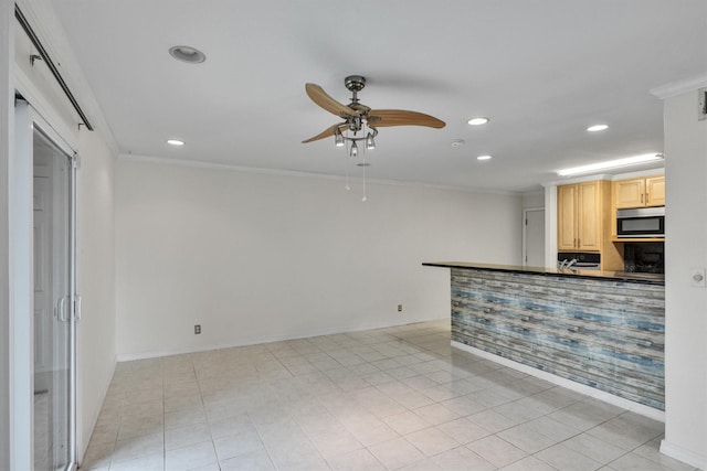 kitchen with light brown cabinets, a ceiling fan, stainless steel microwave, dark countertops, and crown molding