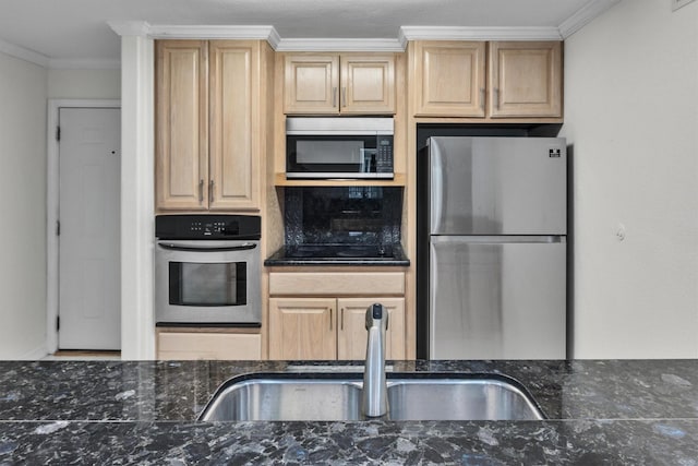 kitchen featuring ornamental molding, appliances with stainless steel finishes, dark stone countertops, and a sink