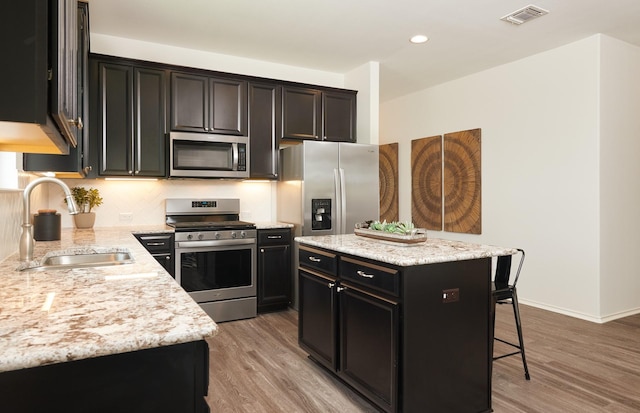 kitchen featuring visible vents, a kitchen breakfast bar, stainless steel appliances, light wood-style floors, and a sink