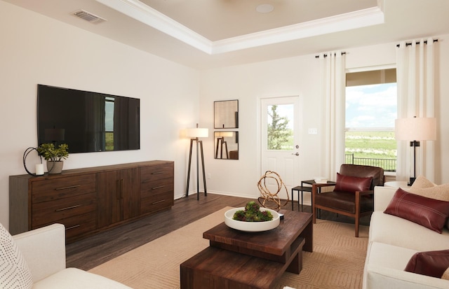 living area with a raised ceiling, visible vents, crown molding, and wood finished floors