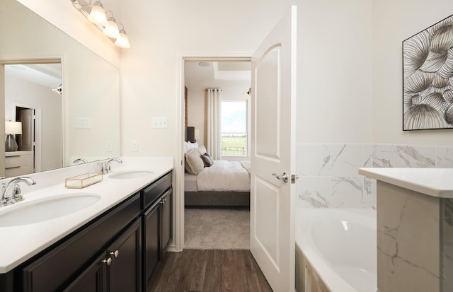 ensuite bathroom with wood finished floors, a garden tub, a sink, and double vanity