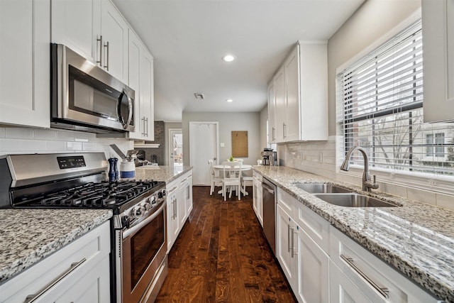 kitchen featuring dark wood-type flooring, a sink, stainless steel appliances, white cabinetry, and backsplash