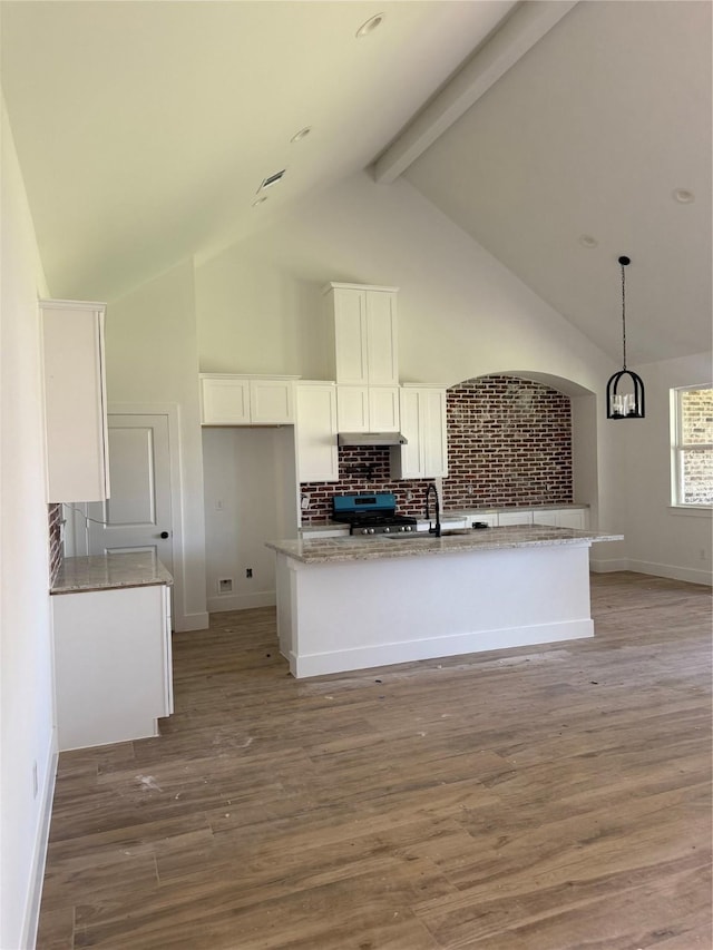 kitchen with a kitchen island with sink, white cabinetry, stainless steel gas range, light wood-type flooring, and beamed ceiling