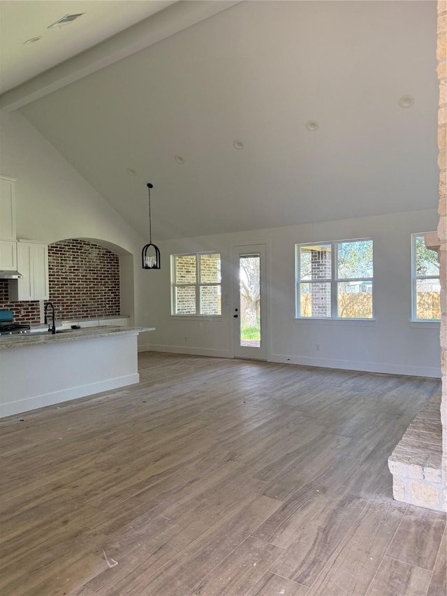 unfurnished living room featuring beam ceiling, visible vents, a sink, and light wood-style flooring