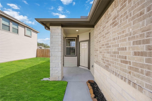 property entrance with fence, a lawn, and brick siding