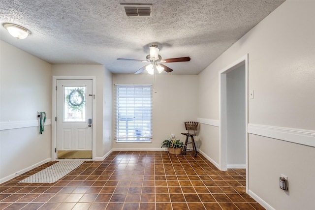 foyer entrance with a textured ceiling, tile patterned flooring, visible vents, baseboards, and a ceiling fan