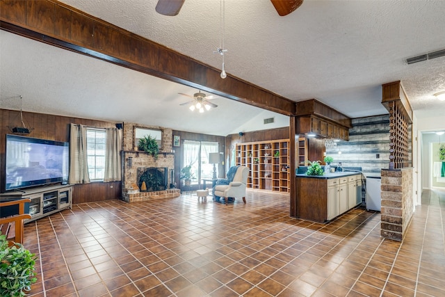 kitchen featuring a ceiling fan, a brick fireplace, plenty of natural light, and wooden walls