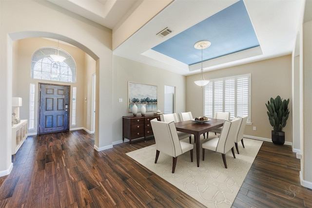 dining area with arched walkways, a tray ceiling, dark wood-type flooring, and baseboards