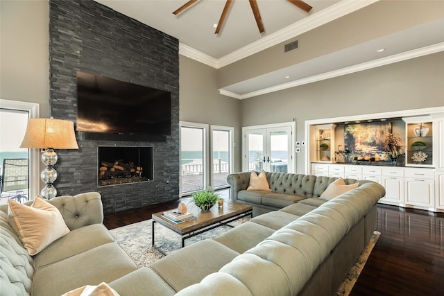 living area with dark wood-style flooring, visible vents, a high ceiling, ornamental molding, and a large fireplace