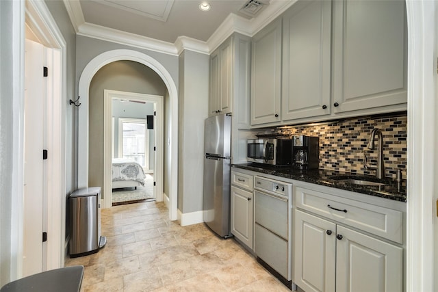 kitchen with arched walkways, stainless steel appliances, a sink, ornamental molding, and decorative backsplash