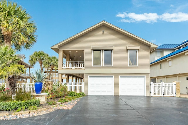 beach home with an attached garage, a gate, fence, a balcony, and driveway