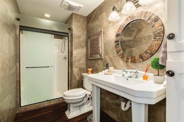 bathroom with visible vents, toilet, hardwood / wood-style flooring, a shower stall, and tile walls