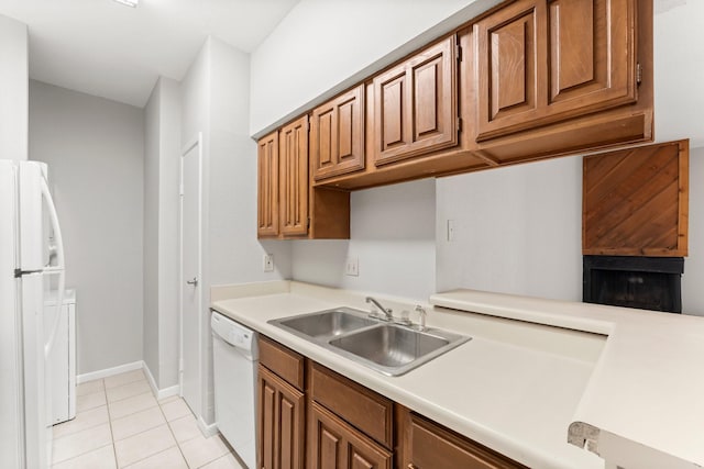 kitchen with light tile patterned floors, light countertops, brown cabinetry, a sink, and white appliances