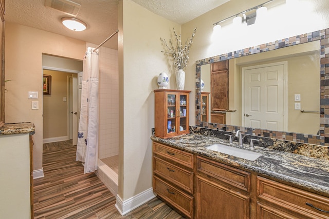 bathroom featuring a textured ceiling, vanity, wood finished floors, tiled shower, and baseboards