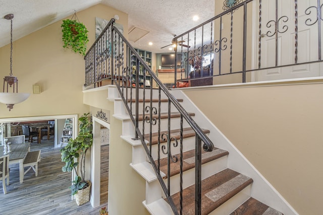 staircase with a ceiling fan, a textured ceiling, wood finished floors, high vaulted ceiling, and baseboards