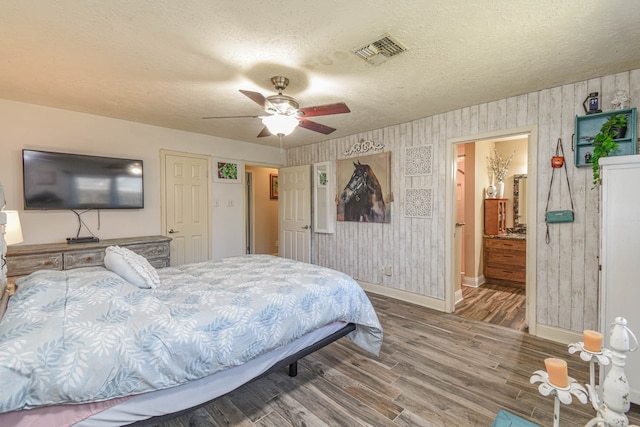 bedroom with visible vents, a textured ceiling, wood finished floors, baseboards, and wallpapered walls