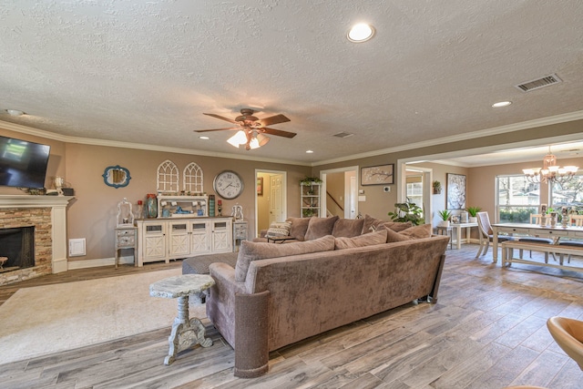 living area with visible vents, wood finished floors, crown molding, a stone fireplace, and ceiling fan with notable chandelier