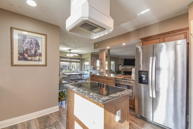 kitchen with a center island, brown cabinets, appliances with stainless steel finishes, a textured ceiling, and wood finished floors