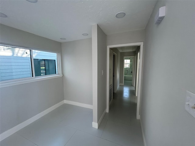 hall with visible vents, light tile patterned flooring, a textured ceiling, and baseboards